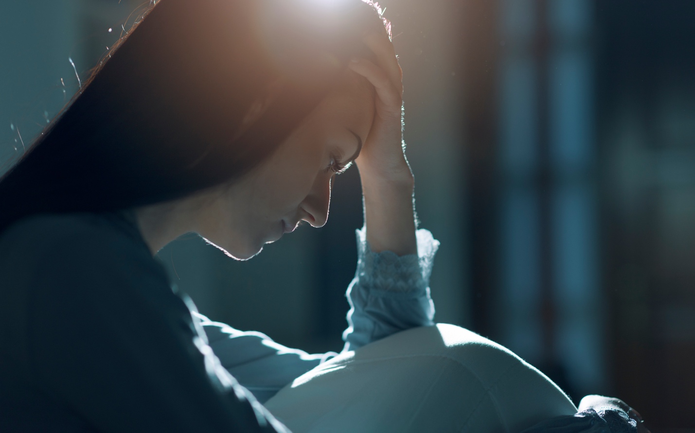 Person sitting with a hand on their forehead in low light